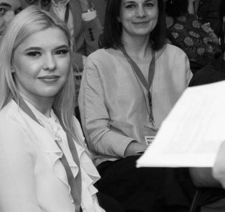 fotografie alb negru, Karina Paval zambitoare, imbracata cu bluza alba, stand pe scaun in timpul unei conferinte