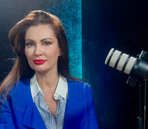 Nicoleta Luciu imbracata cu camasa alba cu dungi albastre si sacou albastru, avand fundal albastru in spatele ei si langa ea aflandu-se un microfon intrucat se pregateste de o noua editie a podcastului ei