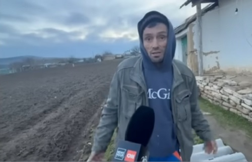 Dumitru Strajeru, tatal suspectului principal in cazul mortii baietelului de 3 ani din judetul Tulcea, barbatul fiind imbracat cu geaca gri si hanorac cu gluga bleumarin, in timp ce da un interviu unui reporter in curtea casei sale