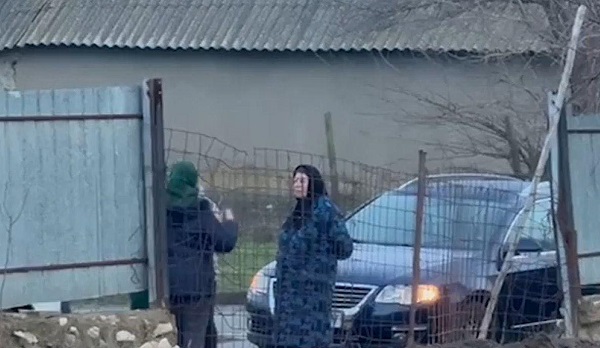 doua femei cu basma pe cap care stau de vorba langa un gard si o masina neagra din apropierea unei case dintr-un sat din comuna Mihai Bravu, județul Tulcea 