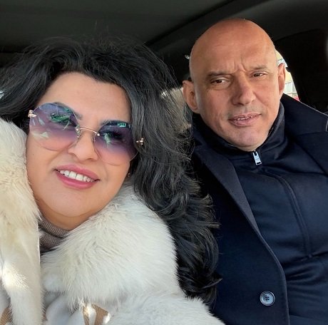 Florin Prunea imbracat cu haine bleumarin stand in masina langa iubita lui, Lacramioara Ursu, zambitoare, purtand ochelari si fiind imbracata cu o haina alba cu guler de blana