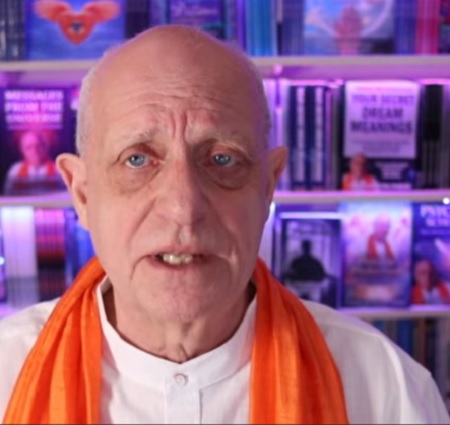 captură video, portret Craig Hamilton-Parker imbracat in alb, cu esarfa portocalie la gat, in timp ce discuta intr-un cadru in care este inconjurat de carti 