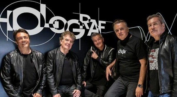 membrii trupei Holograf impreuna, imbracati toti in negru,stand langa un perete negru pe care scrie cu alb numele trupei si pregatindu-se de un concert