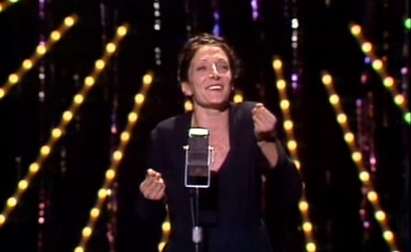 actrița Jane Lapotaire imbracata in rochie neagra, stand in fata microfonului pe o scena cu lumini aurii, imitand-o pe Edith Piaf, prestatie pentru care a primit Premiul Tony