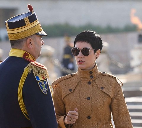 consilier prezidential Delia Dinu cu ochelari negri, imbracata cu jacheta bej, stand in fata unui militar in cadrul unei ceremonii oficiale