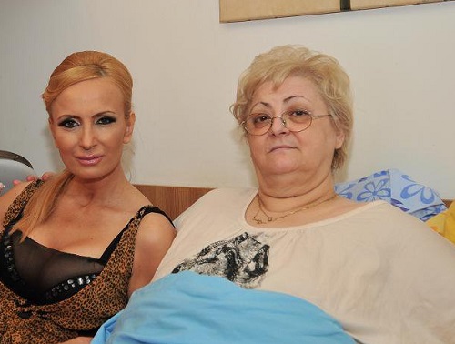 Daniela Gyorfi imbracata in rochie animal print decoltata, cu partea de sus neagra, transparenta, stand pe pat langa mama ei, Anica Dita, care poarta ochelari si o bluza bej cu model negru pe piept