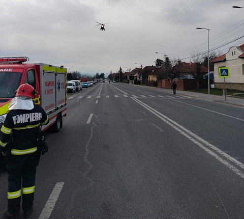 imagine ISU Harghita, pompier SMURD stand cu spatele pe sosea, intr-o zona cu case,langa o masina de pompieri SMURD, in timp ce un elicopter SMURD zboara deasupra 