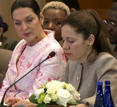 captură YouTube,Mirabela Gradinaru imbracata cu costum bej de stofa, stand pe scaun in fata unui microfon și a unui aranjament floral din flori albe,langa ea aflandu-se o reprezentanta din delegatia Rom&acirc;niei la Summitul de la Washington, si tinand un discurs in cadrul summitului