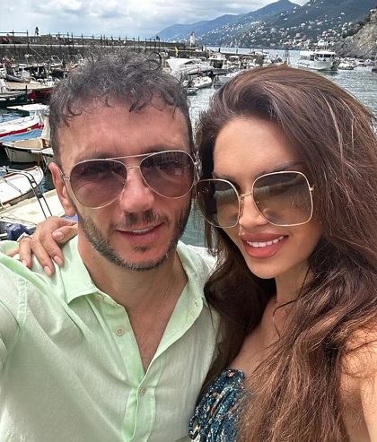 Cristina Spatar cu ochelari de soare, zambitoare, imbracata cu un top sau cu o rochie colorata, in timp ce isi tine mainile pe umerii sotului ei, Vicentiu Mocanu,imbracat cu camasa vernil, amandoi aflandu-se intr-un port turistic in timpul unei vacante in Italia, la Portofino  