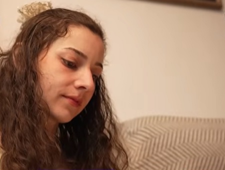 captură video YouTube, Noelia Castillo, tanara care a murit dupa ce a fost eutanasiata, trista, cu privirea in jos, stand pe o canapea bej