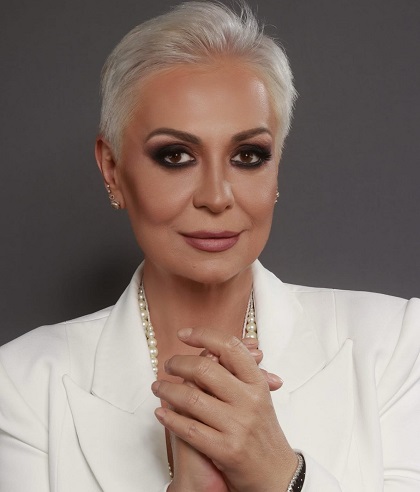 Monica Anghel imbracata in alb, cu colier de perle,cu machiaj smoky eyes, tinandu-si mainile impreunate pe piept