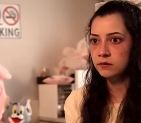 captură YouTube, Noelia Castillo trista, imbracata cu bluza bej, stand in scaunul ei cu rotile, intr-o camera in care se vad jucarii, in timp ce acorda un interviu