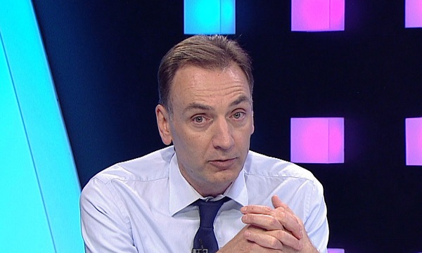Radu Naum imbracat in camasa alba cu cravata albastra, ganditor, tinandu-si palmele stranse, in timp ce se afla in platoul emisiunii Fotbal Club de la Digi Sport
