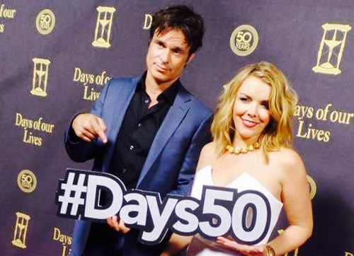 Patrick Muldoon imbracat in costum albastru cu camasa bleumarin alaturi de una dintre colegele sale din productia Days of our Lives, in timp ce stau cu spatele la un perete violet pe care scrie cu auriu &bdquo;Days of our Lives&rdquo; si tin in mana un carton cu &bdquo;Days50&rdquo;