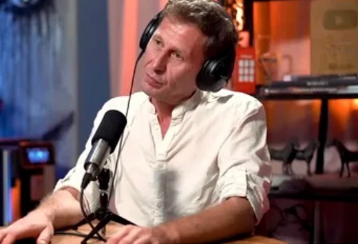 Mircea Solcanu imbracat in camasa alba, ganditor, avand pe cap casti negre, in timp ce sta in fata unui microfon cand a fost invitat la un podcast