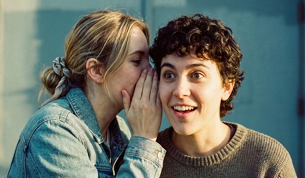 ilustratie, femeie tanara, blonda, cu parul strans, imbracata in geaca de blugi, soptindu-i ceva la ureche unei alte femei, cu parul scurt, cret, imbracata in pulover maroniu, care se mira de ceea ce aude