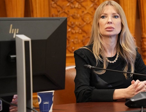 fosta senatoare PSD Victoria Stoiciu, imbracata in negru, purtand un colier aur, tinandu-si palmele incrucisate pe o masa de lemn in timp ce se afla langa un computer intr-un birou din Parlament, in spatele ei aflandu-se pereti acoperiti cu lemn