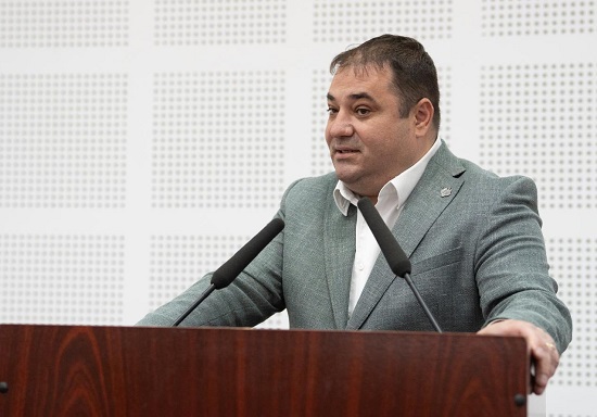 deputatul PSD Adrian Solomon, imbracat in costum gri, cu camasa alba, in timp ce sta la un pupitru cu doua microfoane pentru a lua cuvantul intr-o sedinta