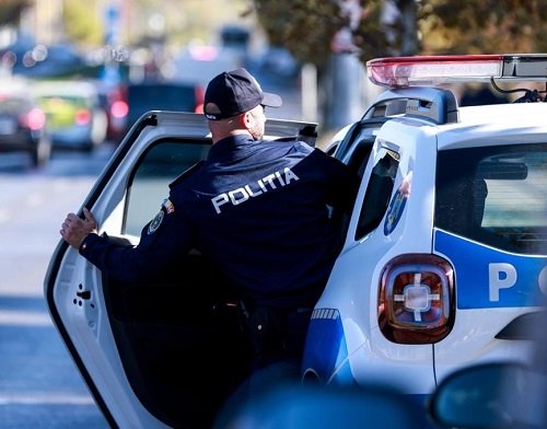 politist in uniforma, cu sapca pe cap,fotografiat cu spatele in timp ce se urca in masina de politie ca sa plece in misiune