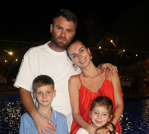 Georgiana Lobonț îmbrăcată cu rochie rosie, cu bretele, sprijinindu-si capul de cel al sotului ei,imbracat cu tricou alb, in timp ce amandoi se afla, impreuna cu copiii lor, intr-o vacanta peste hotare, intr-un cadru nocturn pe marginea unei piscine