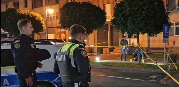 captura video, doi politisti tineri, in uniforma,in misiune noaptea,stand langa masina de politie si uitandu-se la criminalistii care au incercuit locul in care un politist a fost ucis de fiul sau la Piatra Neamt, in fata blocului in care locuia