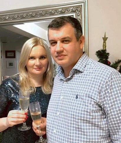 Eugen Tomac imbracat cu camasa alba cu carouri bleumarin, ciocnind un pahar de sampanie cu sotia lui, Diana Postica, imbracata cu bluza sau rochie din lame gri inchis, in timp ce amandoi stau langa un brad de Craciun, cu spatele la o oglinda vintage cu rama argintie