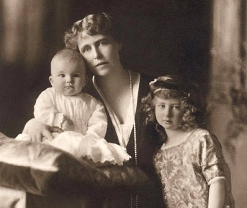 fotografie alb-negru disponibila la Muzeul National Cotroceni, Regina Maria stand pe scaun si lipindu-si fata de cea fiului ei cel mic, care era bebelus, Principele Mircea si avand-o alaturi de ea si pe una dintre fiicele sale, imbracata cu rochita cu maneca scurta