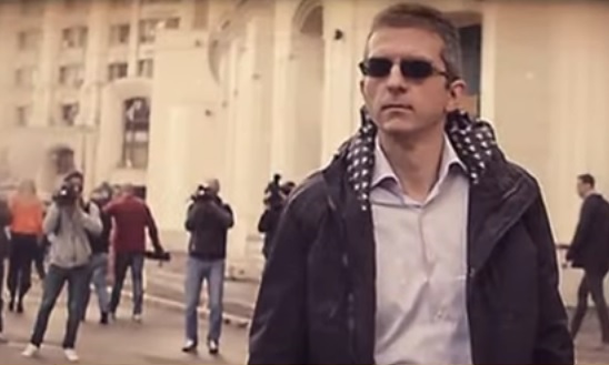 Omul de afaceri Dan Condrea, patronul Hexi Pharma, purtand ochelari negri, imbracat cu camasa si cu jacheta neagra cu gluga, stand in preajma unor blocuri in timp ce este filmat, de la spate, de mai multi jurnalisti