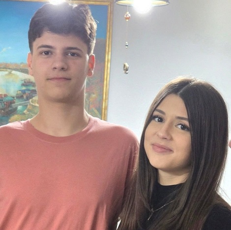 Dragos Florin Tucuina, adolescentul care a murit in urma unui accident cu trotineta electrica, imbracat cu tricou roz, vesel, stand langa sora lui, imbracata in negru, intr-o camera cu tablou pe perete