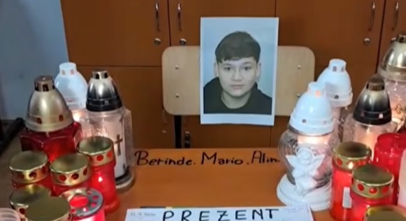 captură video, fotografia lui Mario Berinde, adolescentul de 15 ani din Timis ucis, pusa pe scaunul pe care statea acesta in clasa, iar pe banca fiind mai multe candele si un afis pe care scrie „Prezent”, in spatele bancii aflandu-se un dulap