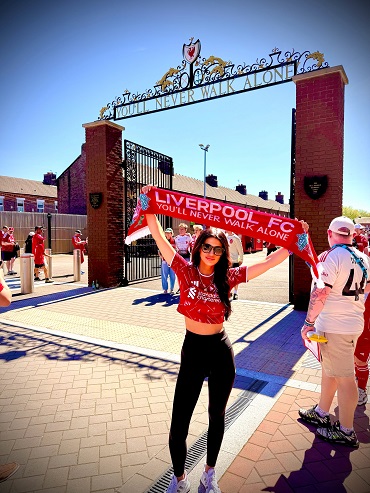 suportera tanara, cu ochelari de soare, imbracata cu tricou rosu si cu colanti negri fluturand un steag cu mesajul „You'll Never Walk Alone” la intrarea in stadionul Anfield din Liverpool, in amintirea tragediei de pe Hillsborough