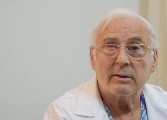 captură video YouTube interviu Gandul, medicul Bogdan Marinescu purtand ochelari, imbracat cu camasa in carouri albastre si roz si cu halat alb, in timpul unui interviu