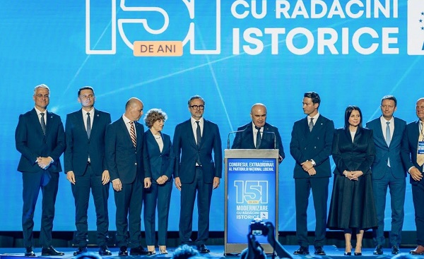 imagine de la Congresul Extraordinar al PNL, la prezentarea motiunii Modernizare cu Radacini, Ilie Bolojan imbracat cu costum bleumarin cu camasa alba si cravata, in timp ce sta la un pupitru cu microfon si tine un discurs, inconjurat de cativa dintre sustinatorii sai
