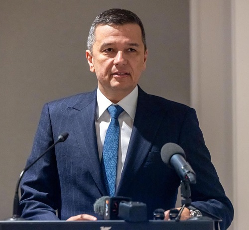 presedintele PSD Sorin Grindeanu imbracat cu sacou albastru, camasa alba si purtand cravata albastra, stand serios la un pupitru cu microfoane in timp ce are un discurs