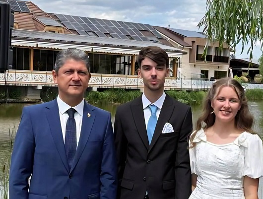 Eliana Bodnariu fericita, imbracata in rochie de mireasa, alaturi de sotul ei, David, imbracat cu costum de culoare inchisa si de Titus Corlatean, imbracat cu costum albastru, toti trei aflandu-se pe malul unui lac, langa complexul la care a avut loc petrecerea de dupa nunta