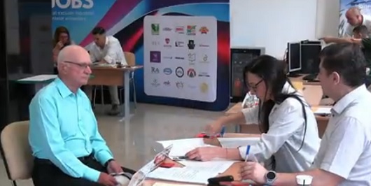 Viorel Pintilescu din Iași, purtand ochelari,imbracat cu camasa vernil si cu pantaloni negri, stand pe un scaun in fata biroului de inscriere la Facultatea de Agricultura din Iasi, specializarea Biologie, in timp ce i se verifica dosarul de inscriere