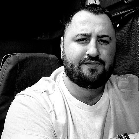 fotografie alb-negru, portret Ionut Marius Cal, romanul de 32 de ani ucis cu lovituri de cutit de alt român, stand pe scaun in camionul sau, imbracat cu tricou si avand bratari la mana