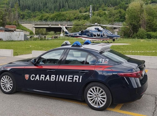 masina de interventie a politiei italiene, carabineri, mergand pe sosea la o interventie si elicopter al Carabinieri, aterizand pe o pajiste intr-o zona de munte cu constructii