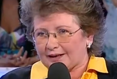 captură video YouTube, Doina Maximilian, fiica adoptiva a Stelei Popescu, imbracata cu bluza galbena si sacou negru, tinand in mana un microfon, purtand ochelari si vorbind in timp ce era invitata la o emisiune TV