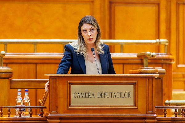 Diana Buzoianu suparata, purtand ochelari, imbracata cu bluza alba si sacou bleumarin, in timp ce sta la pupitru si are o interventie in Parlament, la Camera Deputatilor