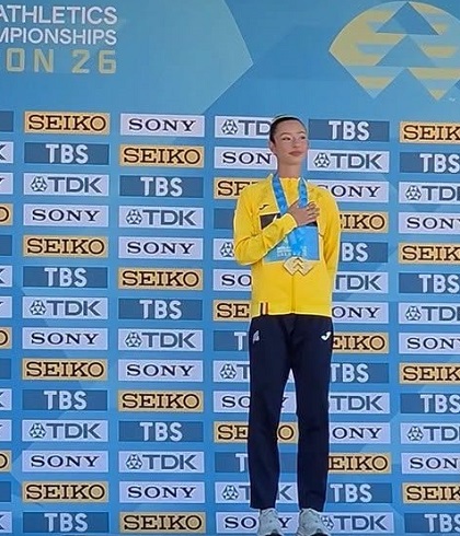 Ștefania Uță &icirc;mbrăcată cu pantaloni bleumarin si cu jacheta galbena, tinandu-si mana pe piept si pe medalia de aur castigata la Campionatele Mondiale de atletism U20, in timp ce se afla pe podium