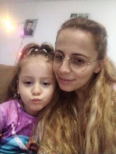 Rebeca, fetita care a murit in accidentul din Moinesti, imbracata cu tricou lila cu bleu, avand o codita in varful capului, in timp ce sta pe o canapea maronie alaturi de mama ei, care poarta ochelari, amandoua aflandu-se intr-o incapere cu peretii albi si cu poze pe pereti