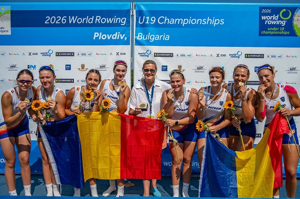 Elisabeta Lipă fericita, imbracata cu camasa alba, tinand in mana o medalie de aur si drapelul României, in timp ce se afla alaturi de fetele care au luat medalii in cadrul Campionatelor Mondiale de juniori de la Plovdiv