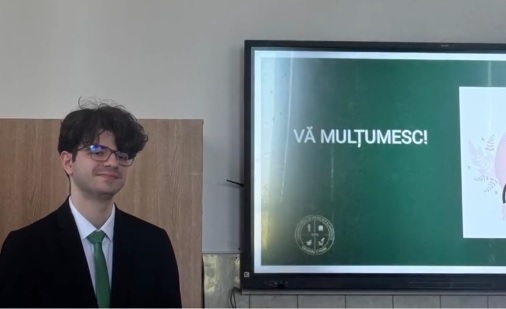 captură video, Calin Vamesu, tanarul care a absolvit Facultatea de Medicina din Iasi cu media 10, purtand ochelari, imbracat cu camasa alba, sacou negru si purtand cravata verde, in timp ce se afla langa un proiector dupa ce a avut o prezentare intr-o sala