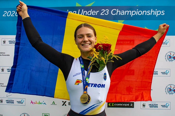 Bianca-Camelia Ifteni, castigatoarea titului european la schif simplu in cadrul Campionatelor Europene de Canotaj Under 23, tinand drapelul Romaniei zambitoare, avand la gat medalia si la piept buchetul de trandafiri rosii primit la festivitatea de premiere 