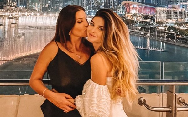 Victoria Lungu, imbracata cu rochie neagra cu bretele subtiri, sarutandu-si pe obraz fiica, Valerie Lungu, vesela, imbracata cu rochie alba decoltata, cu umerii dezgoliti, in timp ce amandoua se afla pe o terasa din Dubai seara