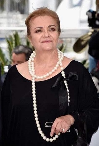 actrița Dana Dogaru zambitoare, imbracata cu rochie neagra de catifea, cu sirag lung de perle, tinand in mana o pereche de ochelari in timp ce se afla la un eveniment