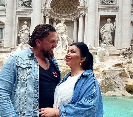 Adriana Bahmuteanu zambitoare, imbracata cu bluza alba si camasa de blugi, in timp ce se uita la George Restivan, imbracat cu tricou negru si jacheta de blugi, amandoi aflandu-se langa o fantana din Roma