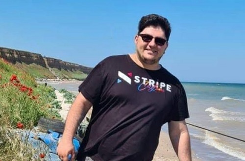 Edy Iorga, fiul cel mare al lui Leo Iorga, zambitor, purtand ochelari de soare negri, tricou negru, in timp ce se afla pe un deal cu maci de la malul marii