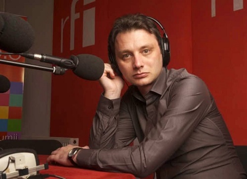 Luca Niculescu ganditor, purtand casti, stand in fata unui microfon, imbracat cu camasa maro cu maneca lunga, in timp ce lucra la Radio France Internationale acum mai multi ani
